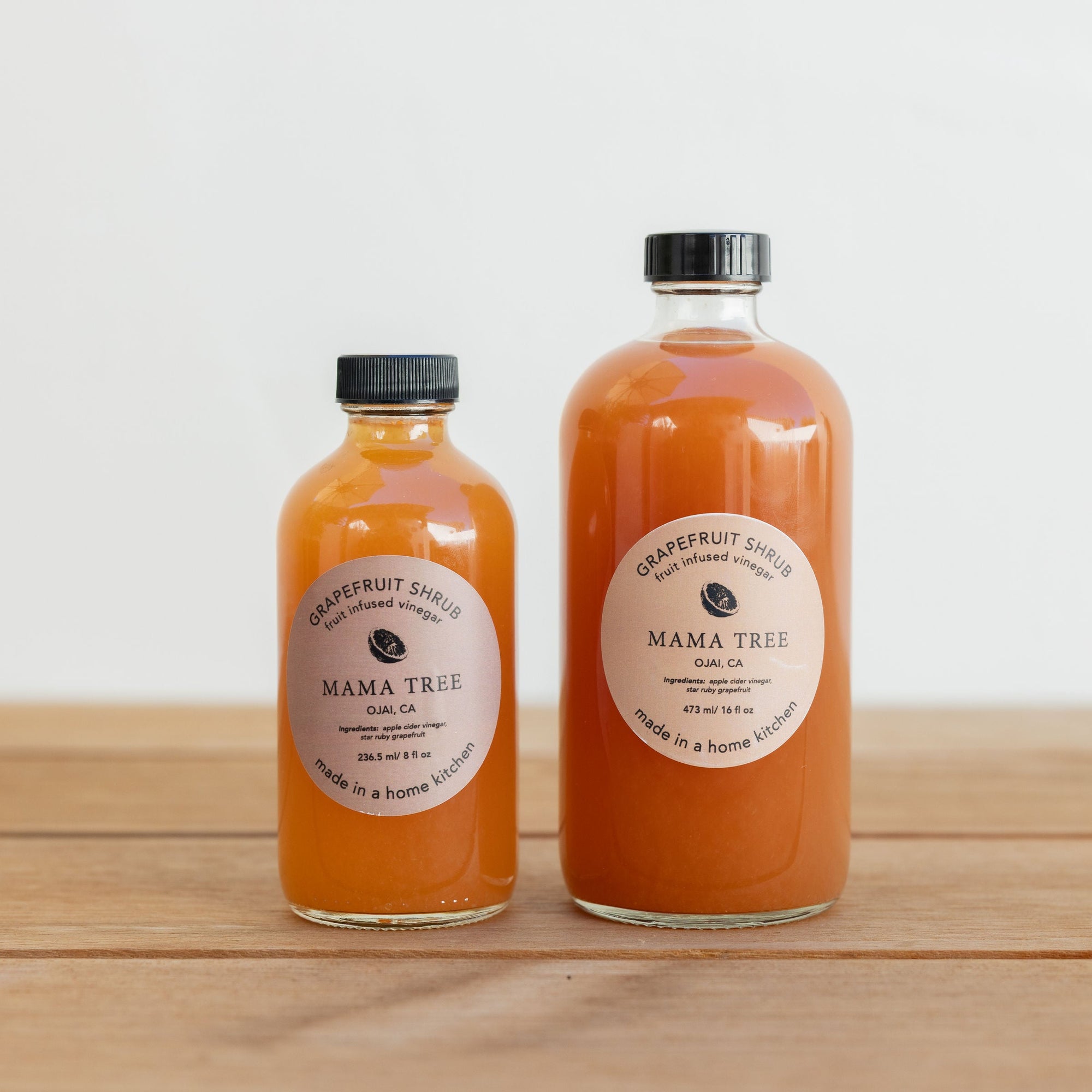 Two bottles of Mama Tree juice on a wooden surface with a white background