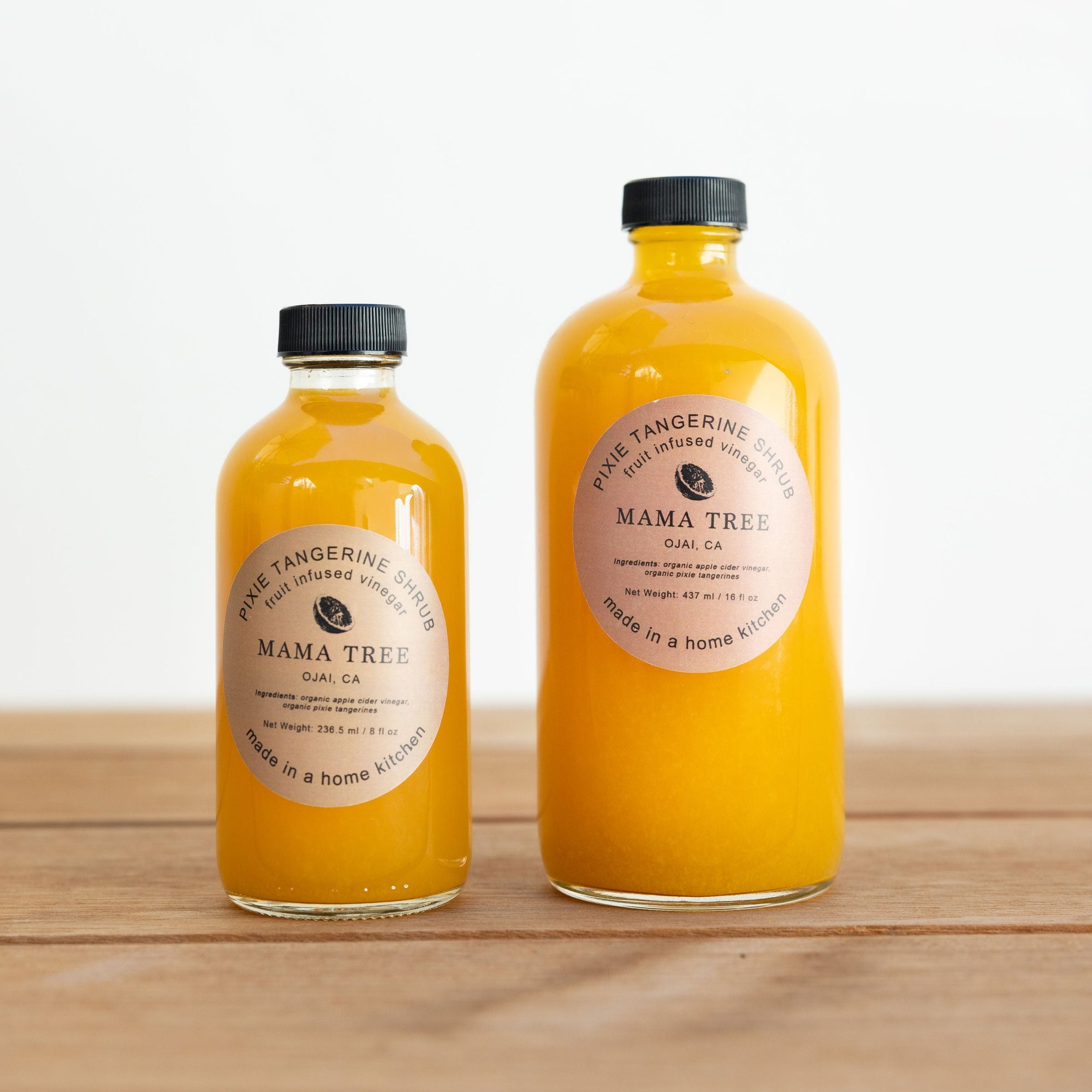 Two bottles of Mama Tree juice on a wooden surface with a white background