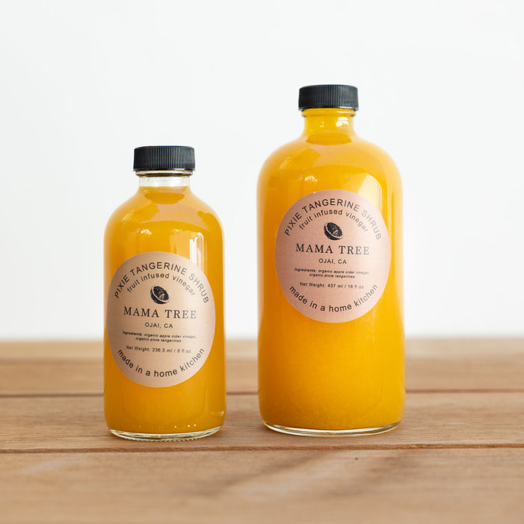 Two bottles of Mama Tree juice on a wooden surface with a white background