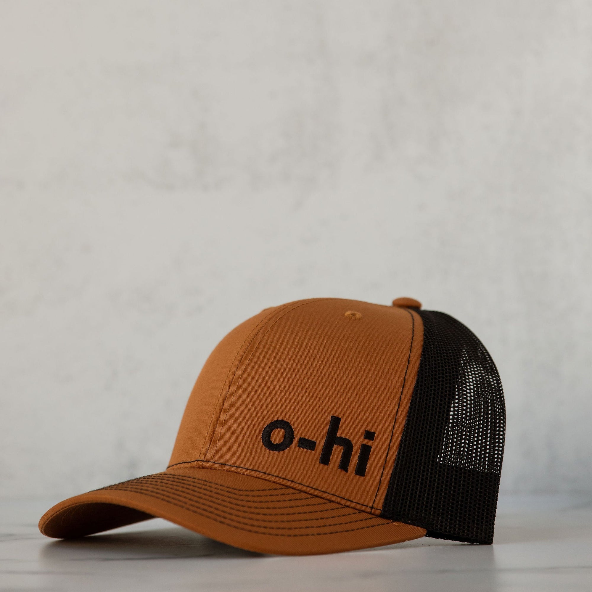 A brown and black o-hi baseball cap with breathable mesh fabric and an adjustable back, displayed against a neutral background.