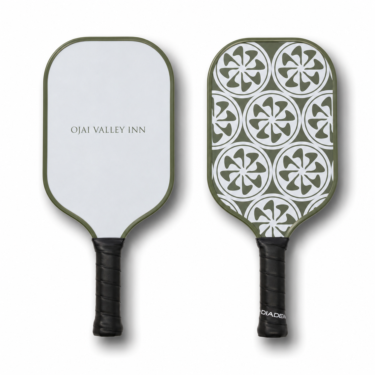 Two pickleball paddles shown side by side on a white background. The left paddle has a white face with an olive green border and the text 'OJAI VALLEY INN' in the center.