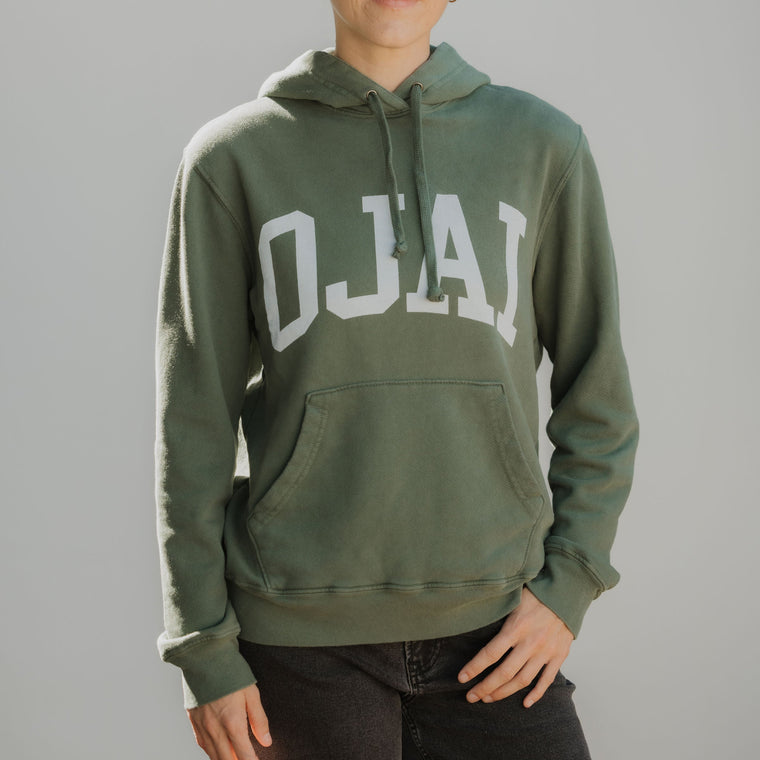 Person wearing a green hoodie with 'OJAI' printed on it against a plain background