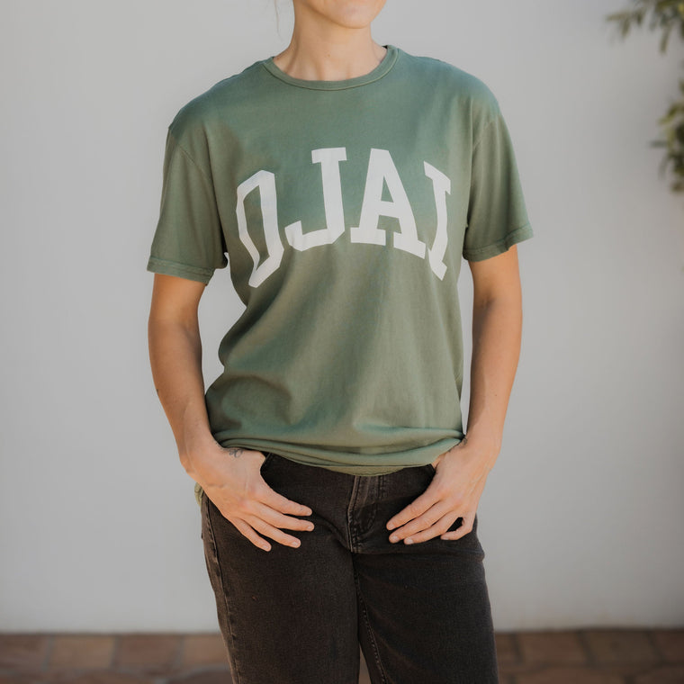 Person wearing a green t-shirt with 'OJAI' printed on it against a white wall.