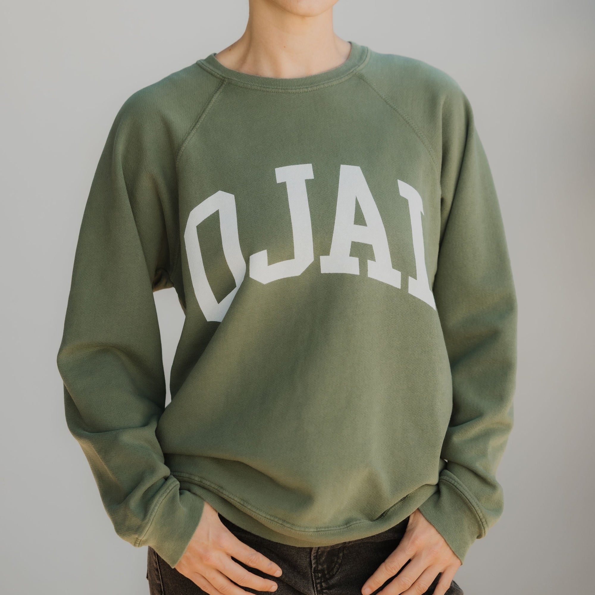 Person wearing a green sweatshirt with 'OJAI' printed on it against a plain background