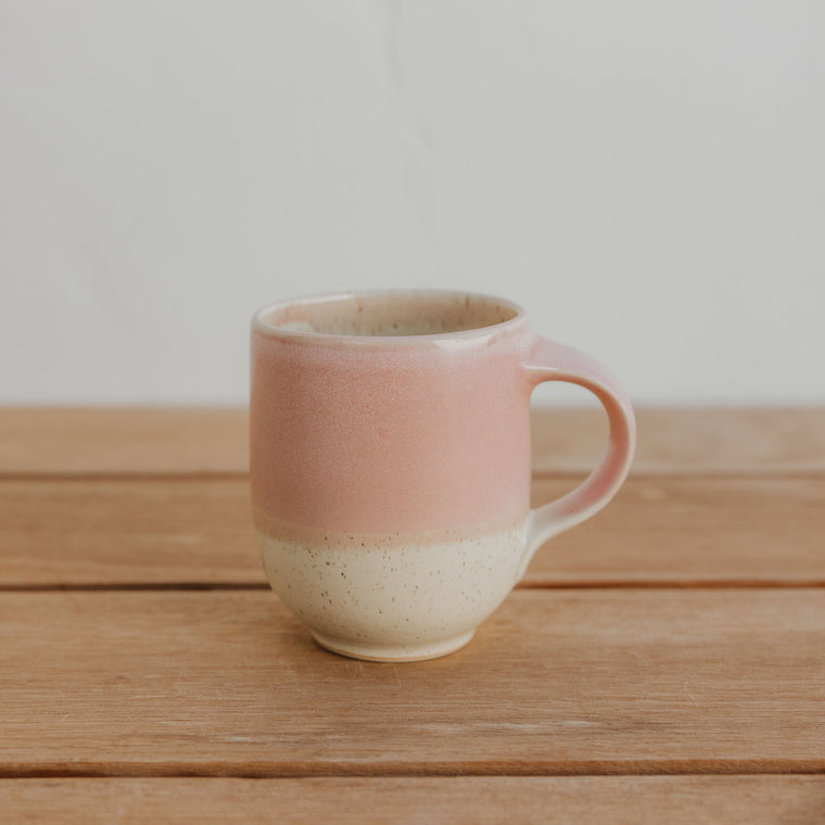 Pink ceramic mug on a wooden surface with a plain background