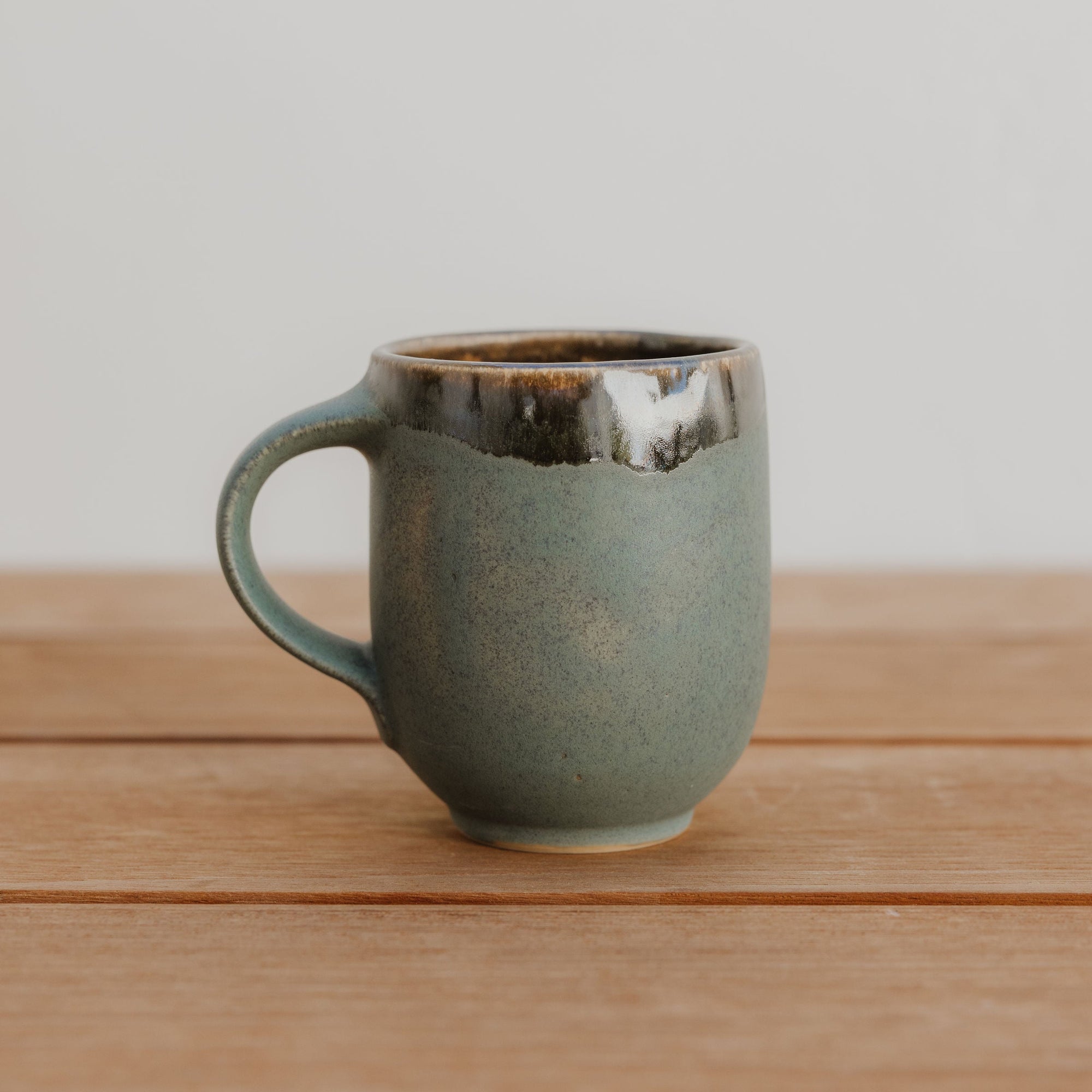 Green ceramic mug on a wooden surface with a plain background