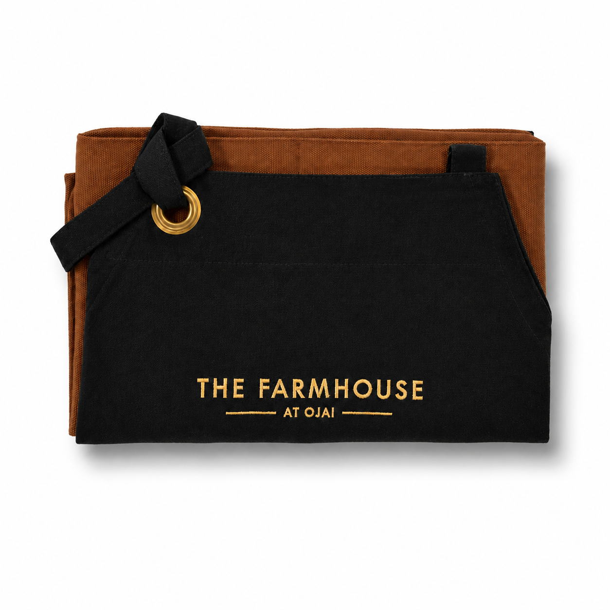 A black canvas apron with gold lettering reading 'THE FARMHOUSE AT OJAI' and a brown suede-like backing, shown on a white background.
