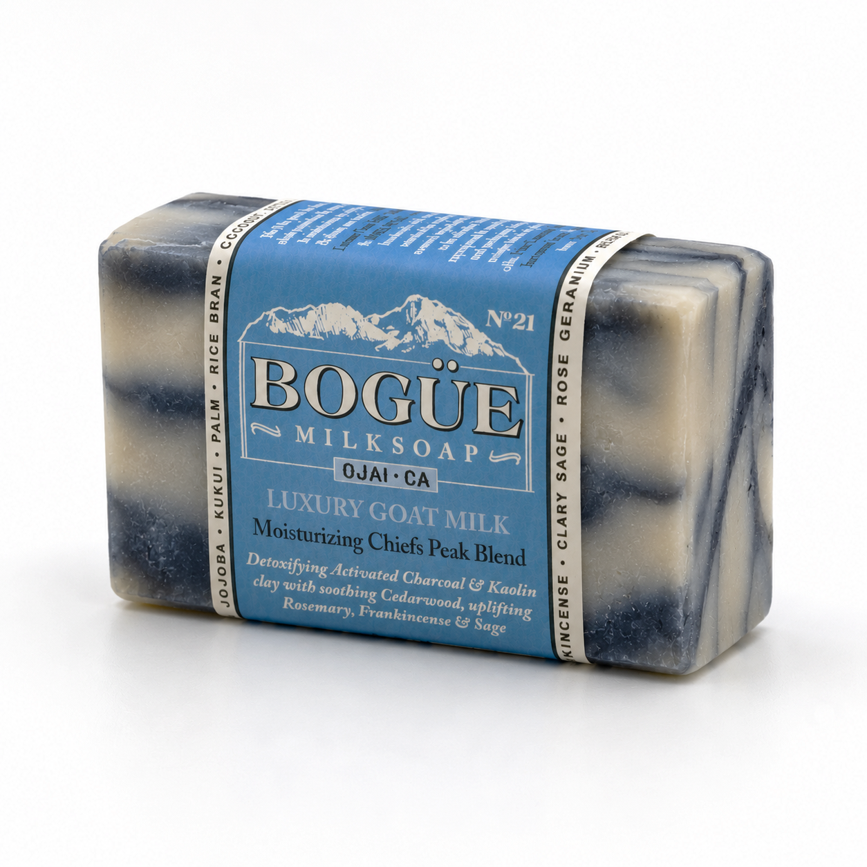 A rectangular bar of Bogue Milksoap with a blue paper label, photographed on a clean white background. The soap itself has a marbled pattern of dark charcoal gray, navy, and cream.