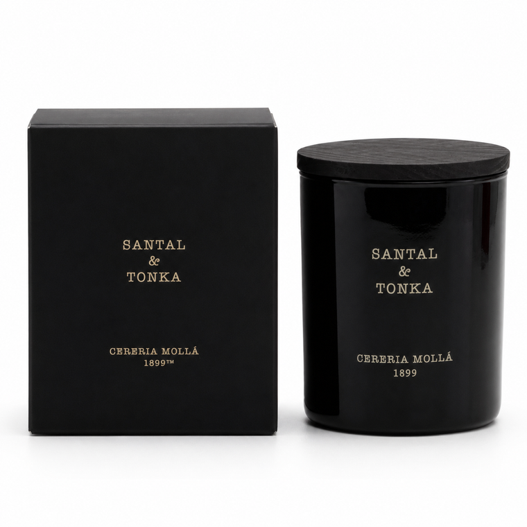 A black scented candle jar with a matching black lid stands next to its black packaging box. Both pieces feature gold lettering that reads 'SANTAL & TONKA' and 'CERERIA MOLLÁ 1899'.