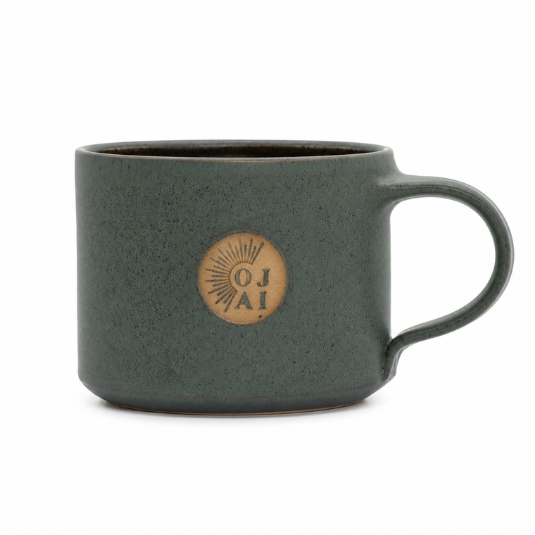 A speckled dark green ceramic mug with a circular tan logo on the front that reads 'OJ AI' with a sunburst design, set against a plain white background.
