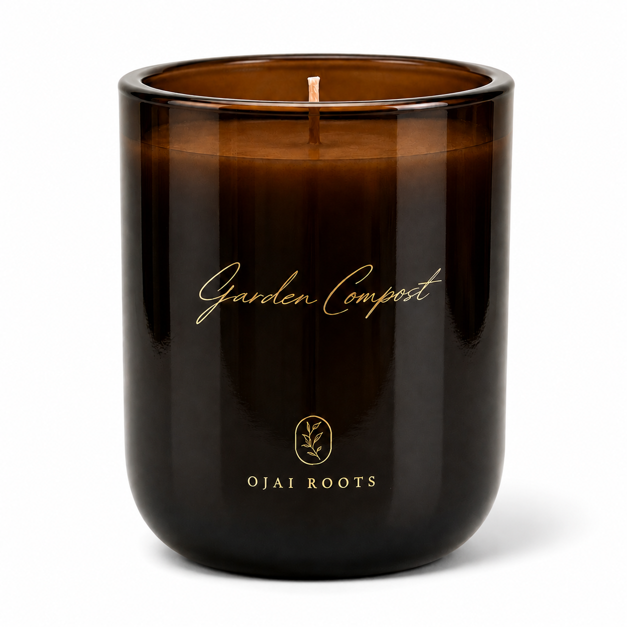 An amber glass jar candle with a single wick, featuring gold foil text that reads 'Garden Compost' and 'OJAI ROOTS' on a clean white background.
