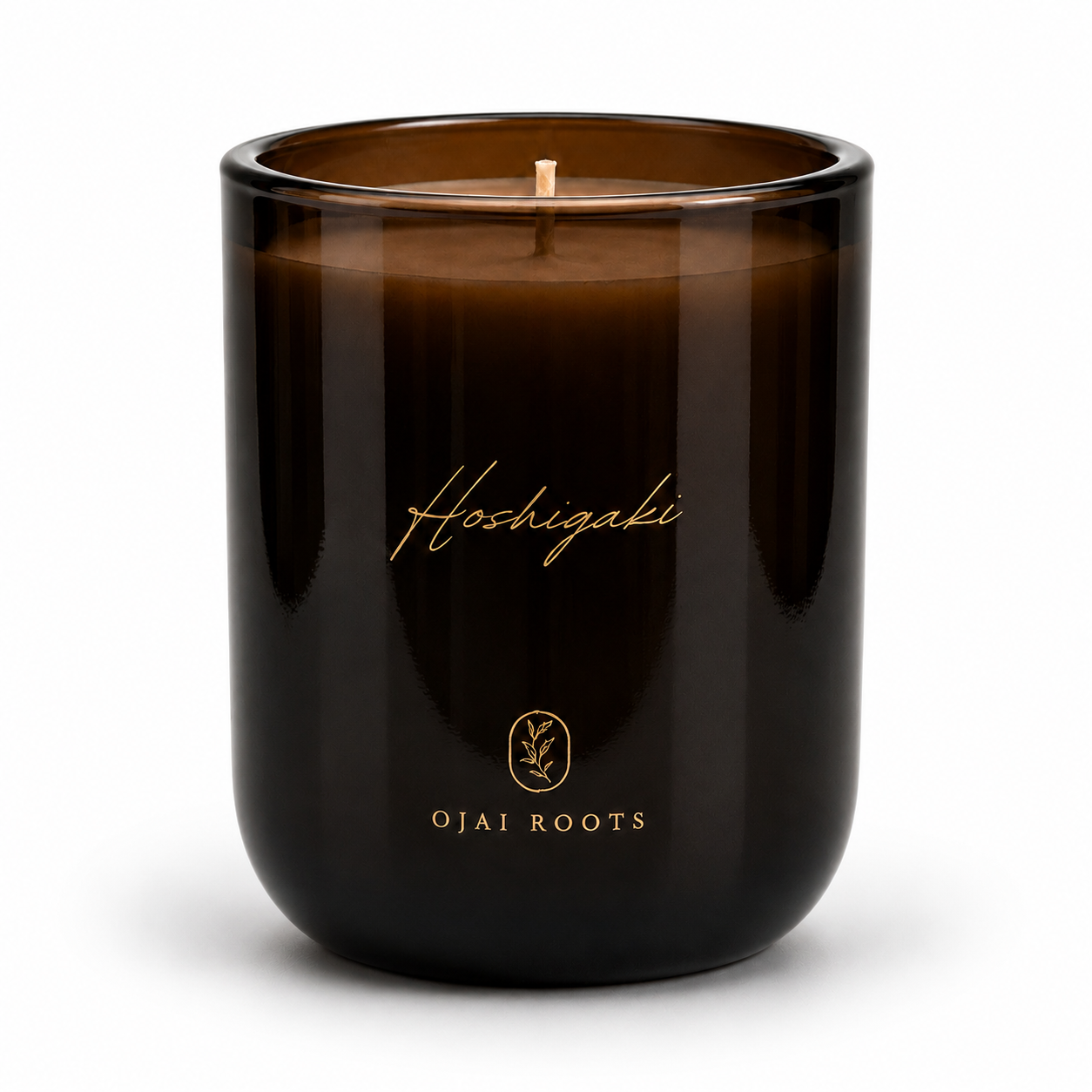 An amber glass jar candle with a single wick, featuring gold foil branding that reads 'Hoshigaki' and 'OJAI ROOTS' on a clean white background.