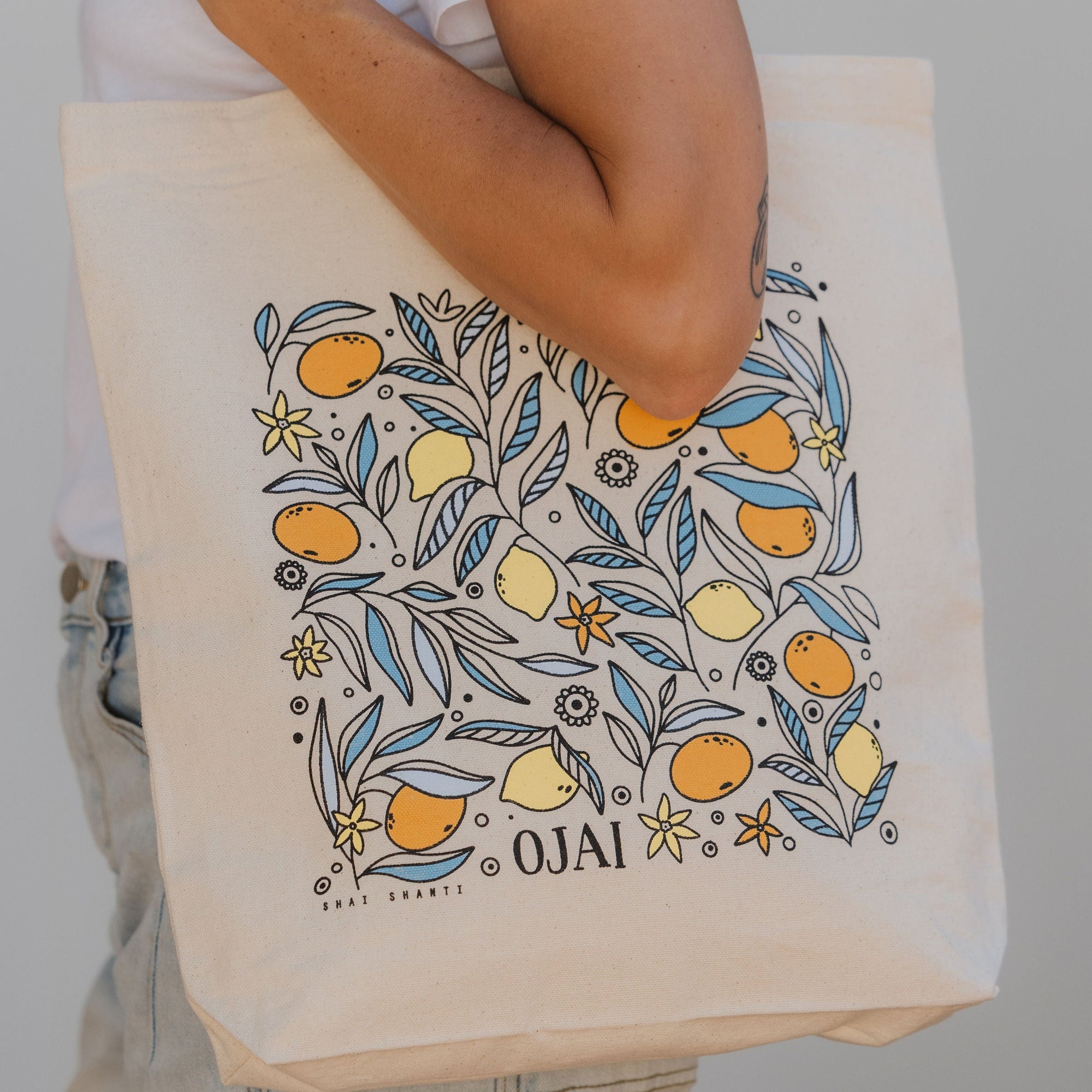 Person holding a tote bag with 'Ojai' design featuring lemons and flowers.