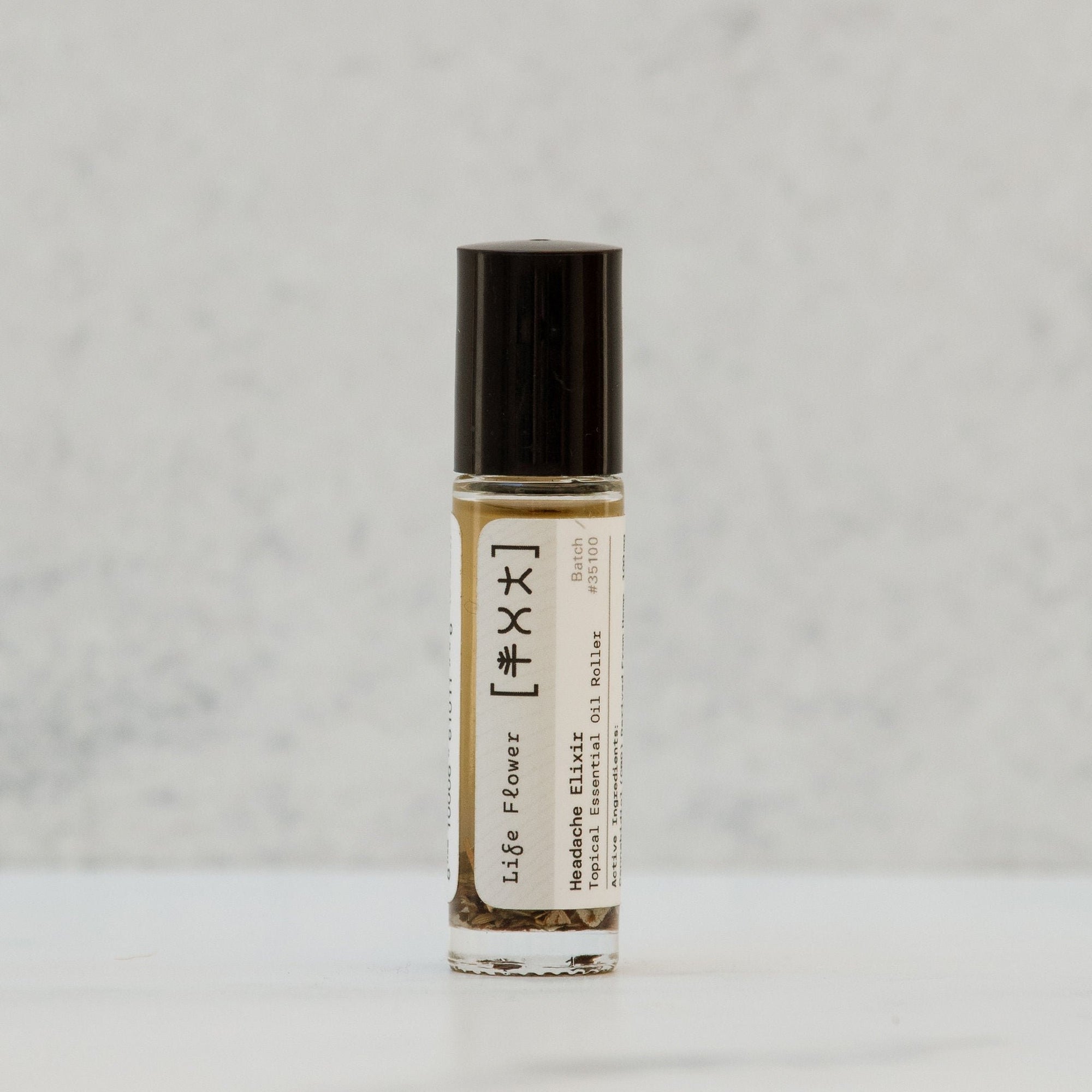 A glass bottle containing a yellowish liquid with a black cap, labeled with 'Life Flower Headache Elixir' and other product details.