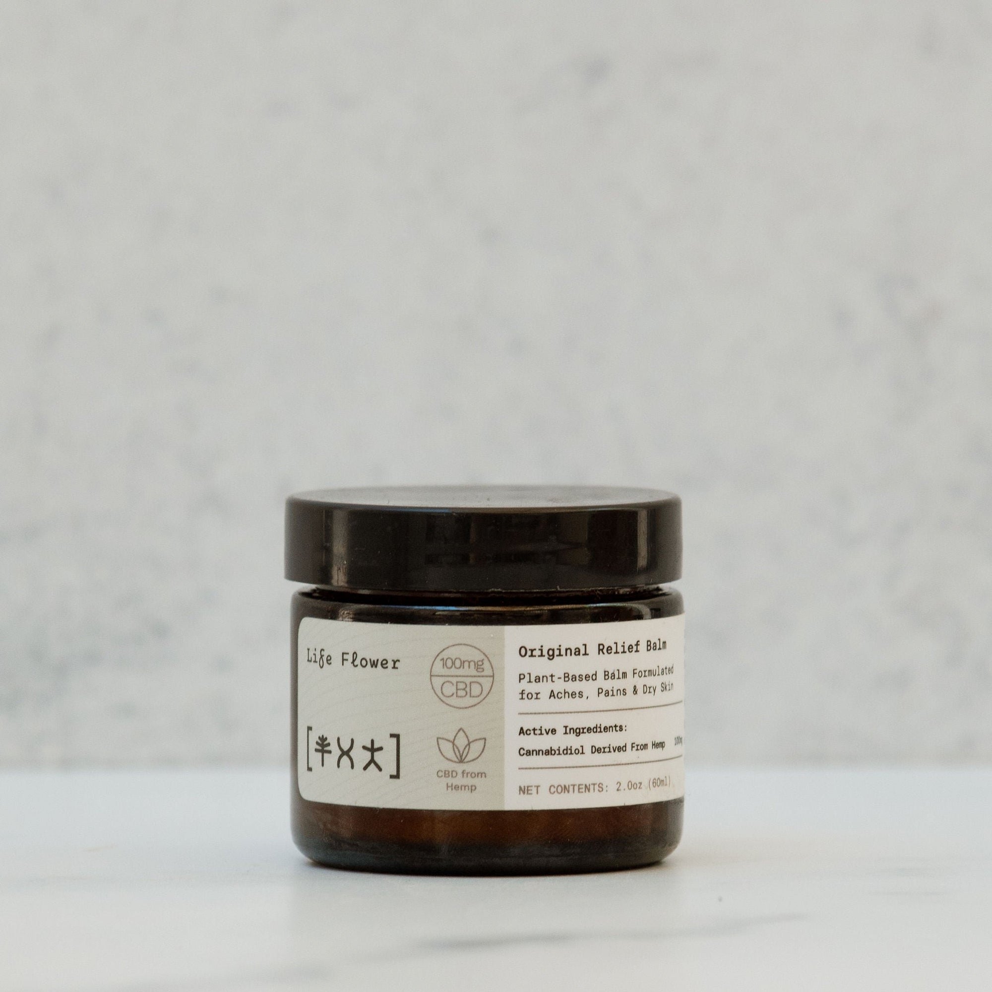 Small amber glass jar that says 'life flower original relief balm' against a neutral background
