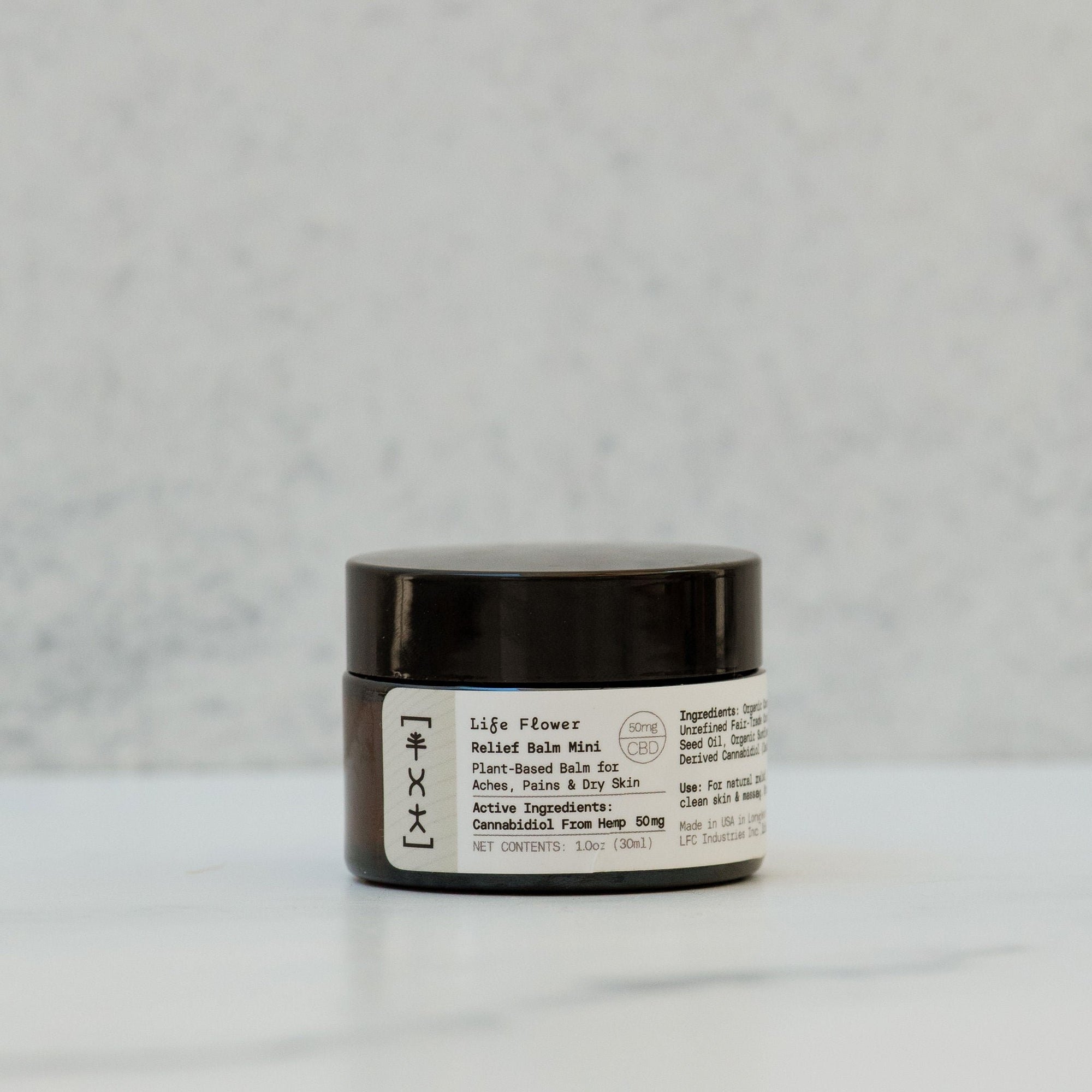 A jar of Life Flower Relief Balm Mini with labels detailing organic coconut oil, olive oil, beeswax, shea butters, and essential oils.