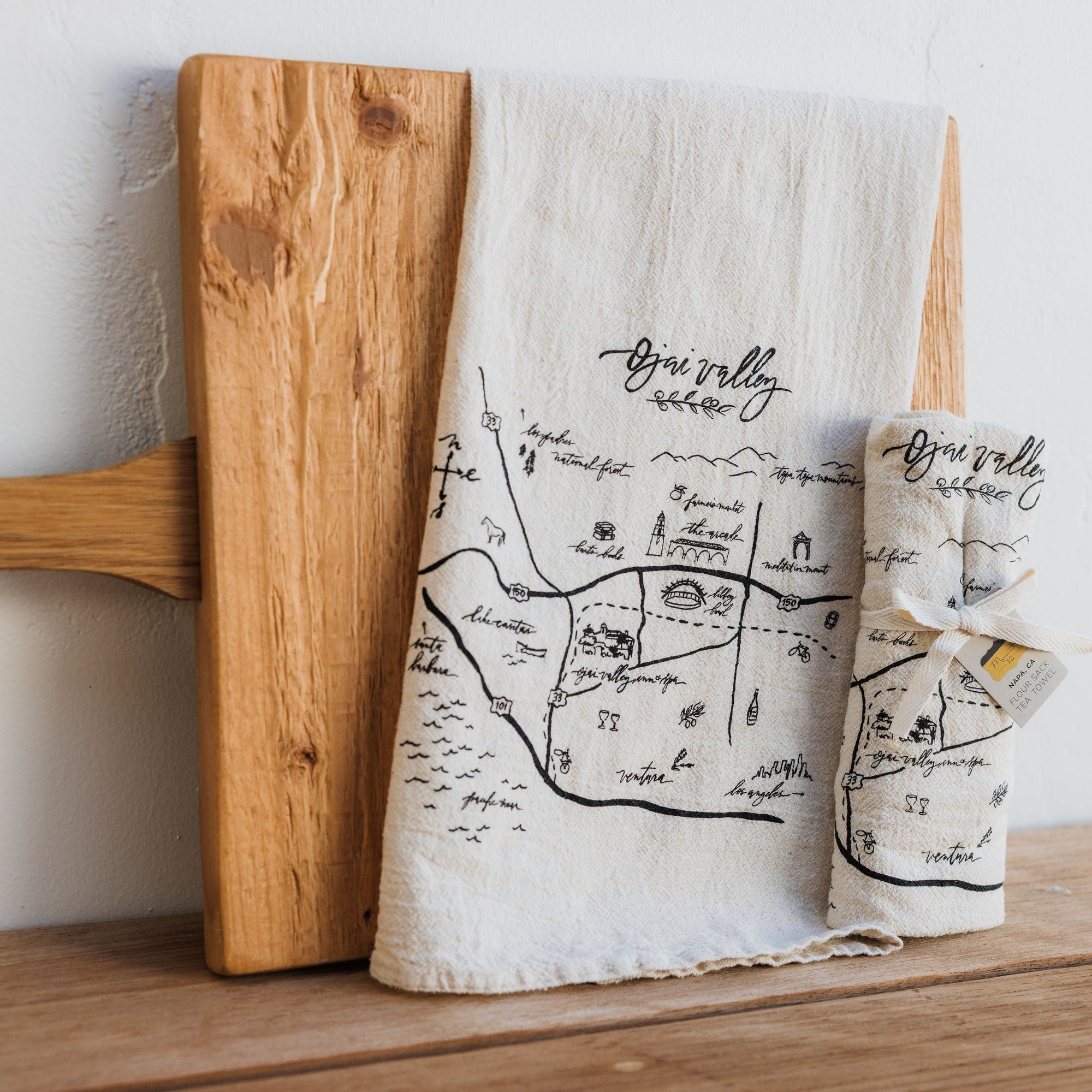 Tea towel with map design and wooden cutting board on a shelf