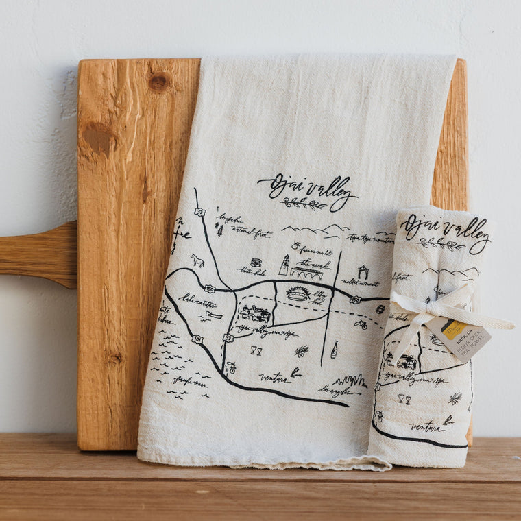 Tea towel with map design on a wooden cutting board against a white background