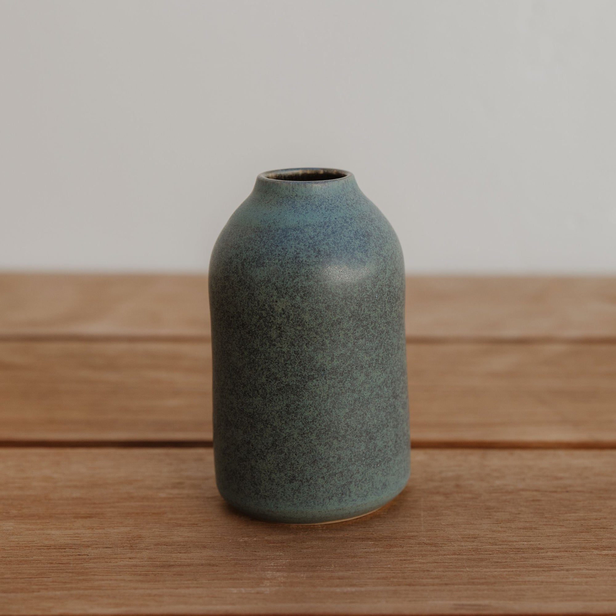 Green ceramic vase on a wooden surface with a plain background