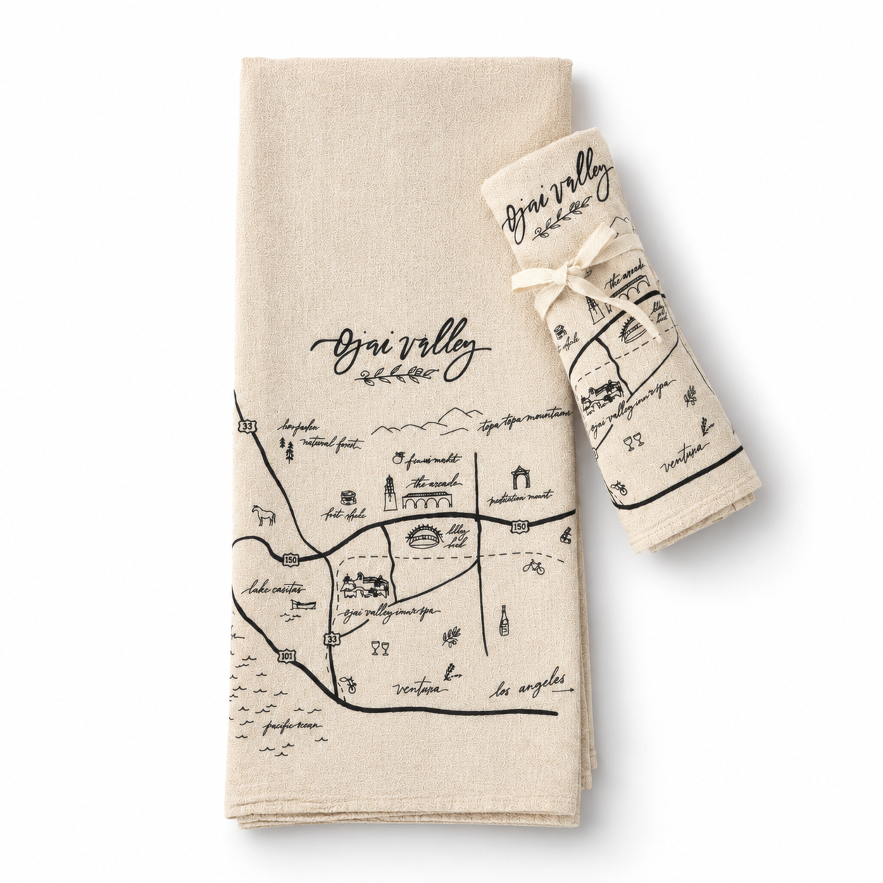Two beige linen kitchen towels with black map-style illustrations and the words 'Bri valley' are shown on a clean white background. One towel is laid flat, and the other is rolled and tied with a ribbon.