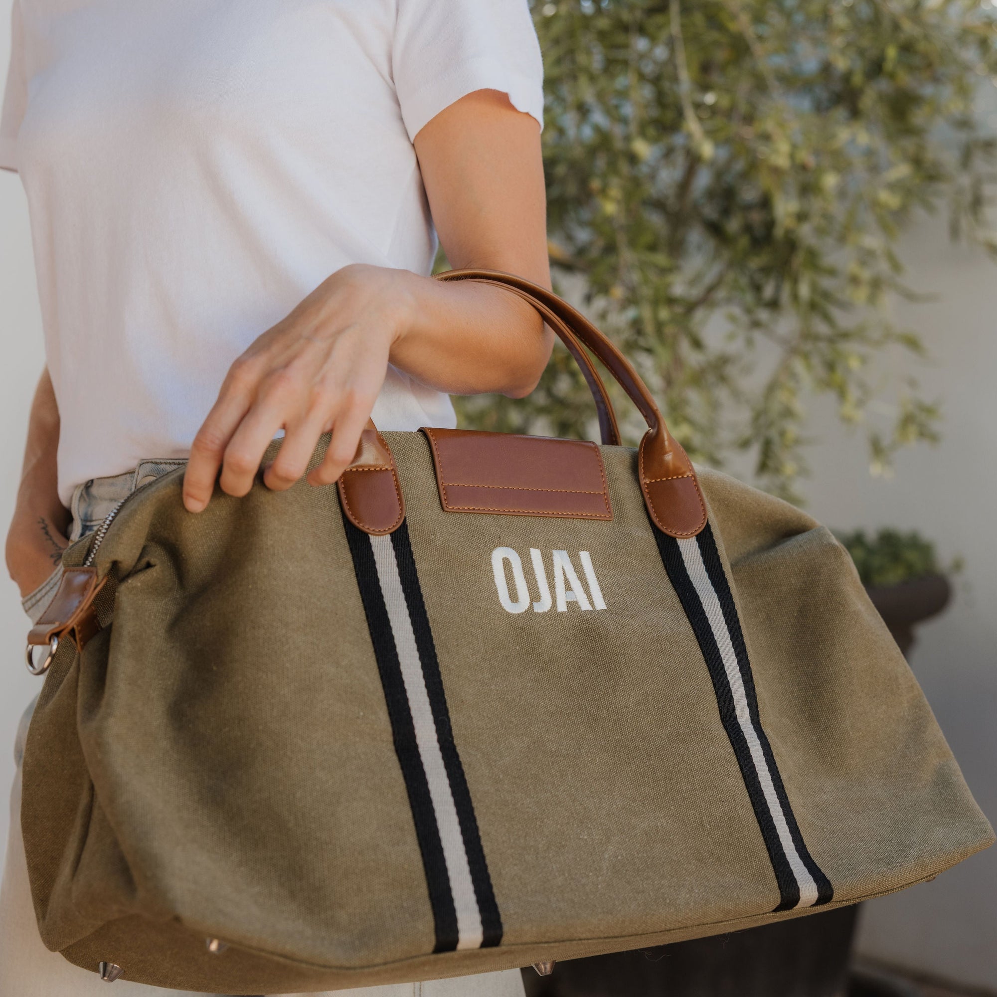 Person holding a brown bag with 'OJAI' branding against a blurred background
