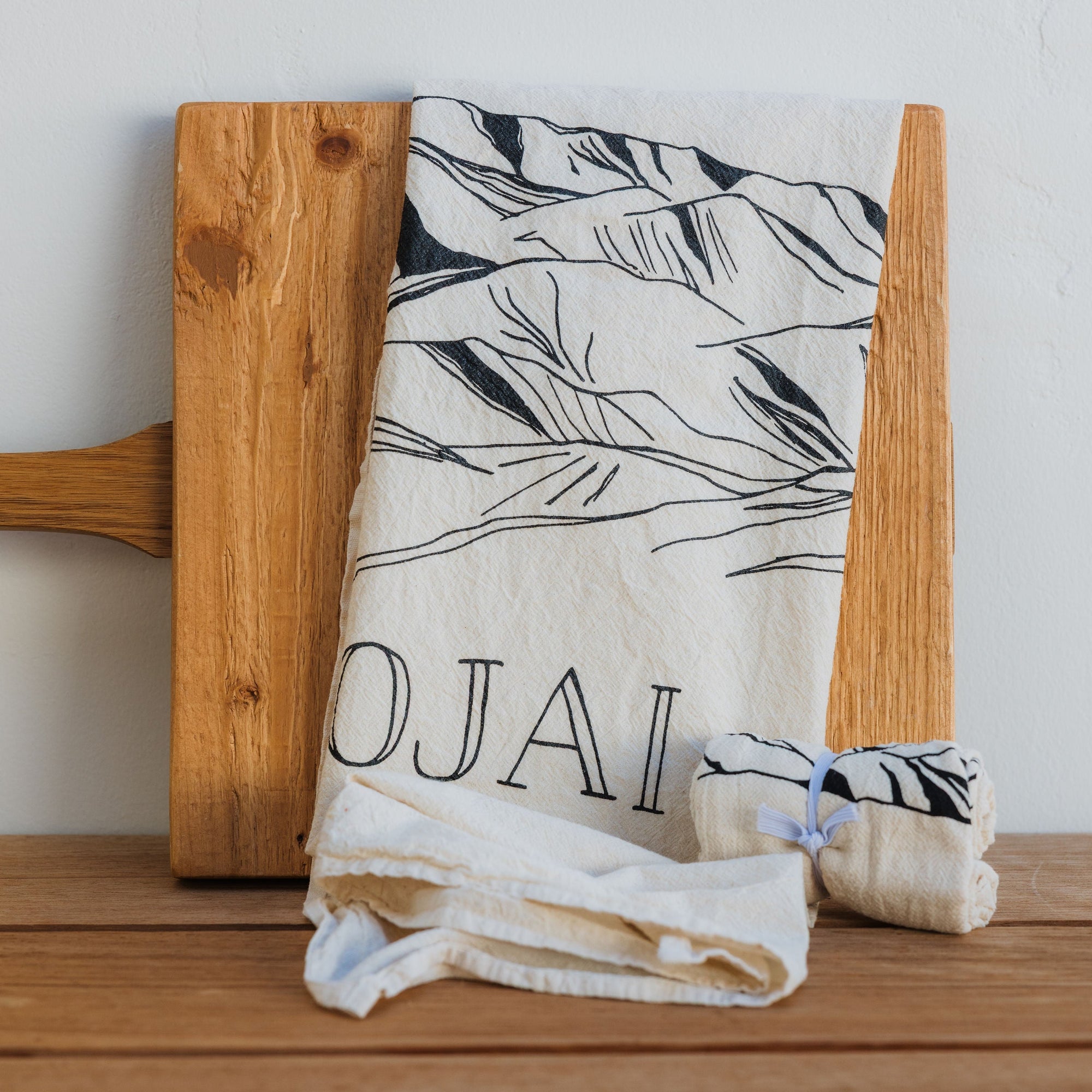 Wooden cutting board with a folded towel featuring 'Ojai' on a wooden surface.