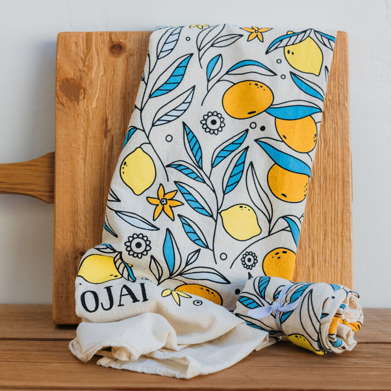 Fabric with lemon pattern draped over a wooden cutting board on a wooden surface.