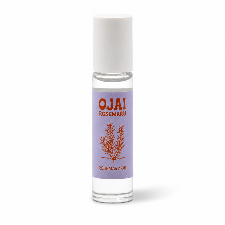 A clear glass roller bottle filled with rosemary oil, featuring a lavender label with red text reading 'OJAI ROSEMARY' and a rosemary illustration, topped with a white cap on a white background.