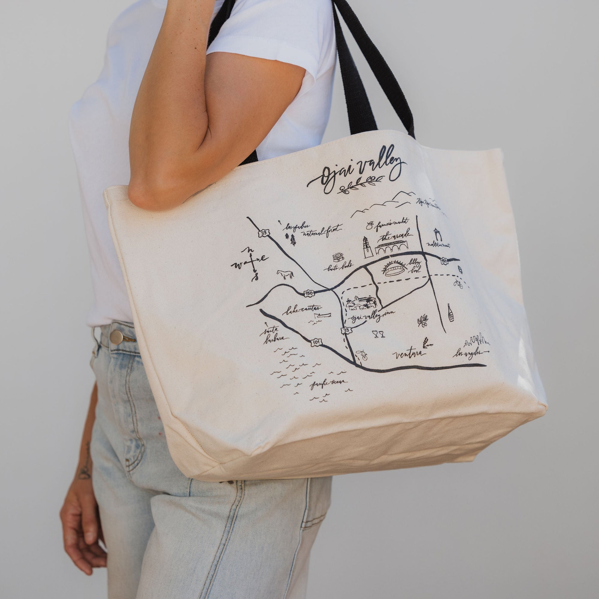 Person holding a tote bag with an Ojai  map design against a plain background