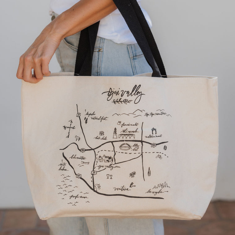 Person holding a tote bag with an Ojai map design and text.