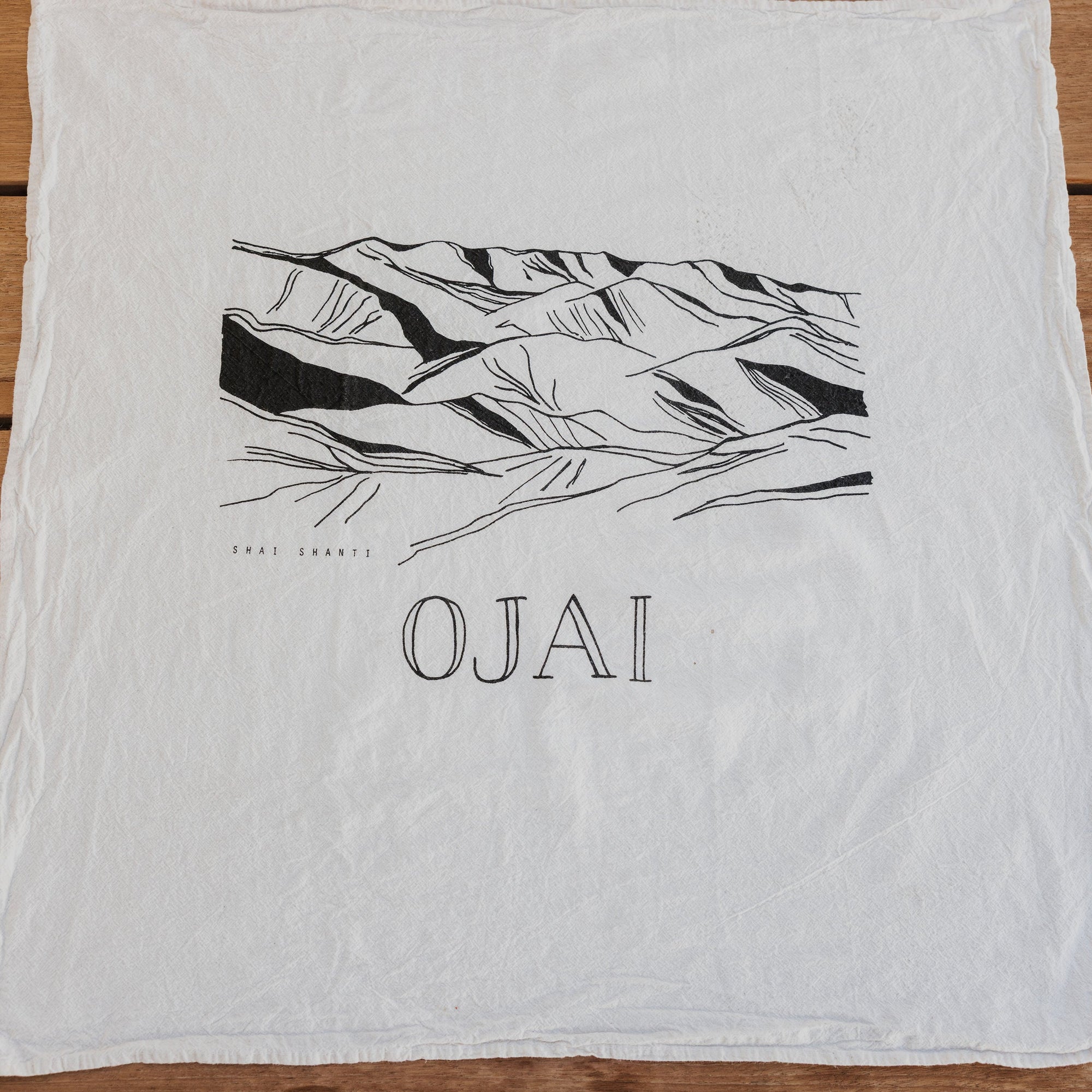 White towel with black mountain graphic and 'Ojai' text on a wooden surface