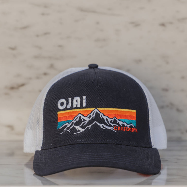 Black and white cap with mountain design and 'Ojai' text on a wooden surface