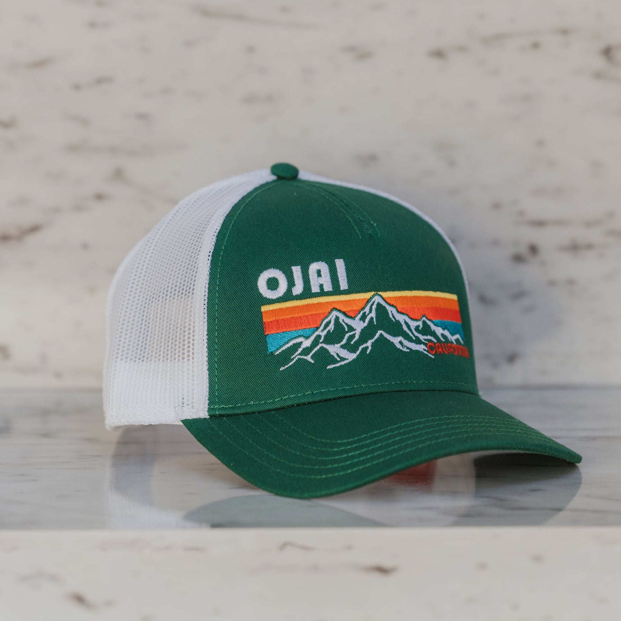 Green and white cap with 'Ojai' logo on a light wooden surface