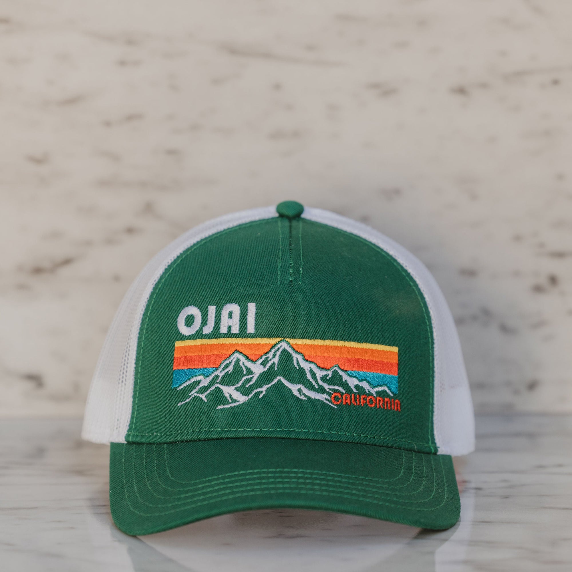 Green and white cap with mountain design and 'Ojai' text on a wooden surface