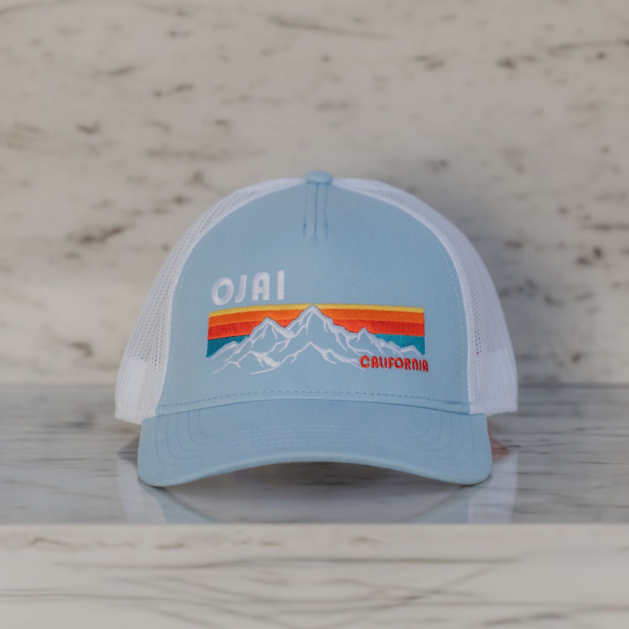 Light blue cap with mountain design and 'Ojai California' text on a marble surface.