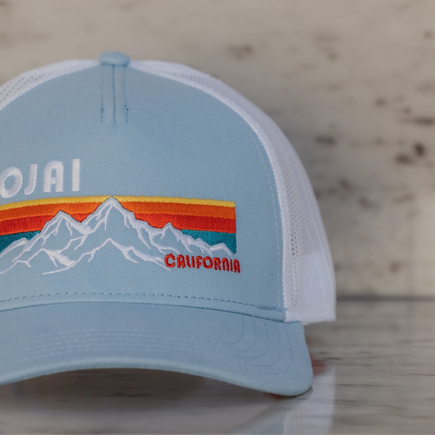 Light blue cap with mountain design and 'Ojai California' text on a wooden surface