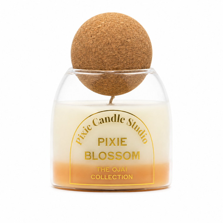 Pixie Candle Studio Pixie Blossom scented candle in a clear glass jar with an orange-to-cream gradient wax, topped with a cork ball on a white background.