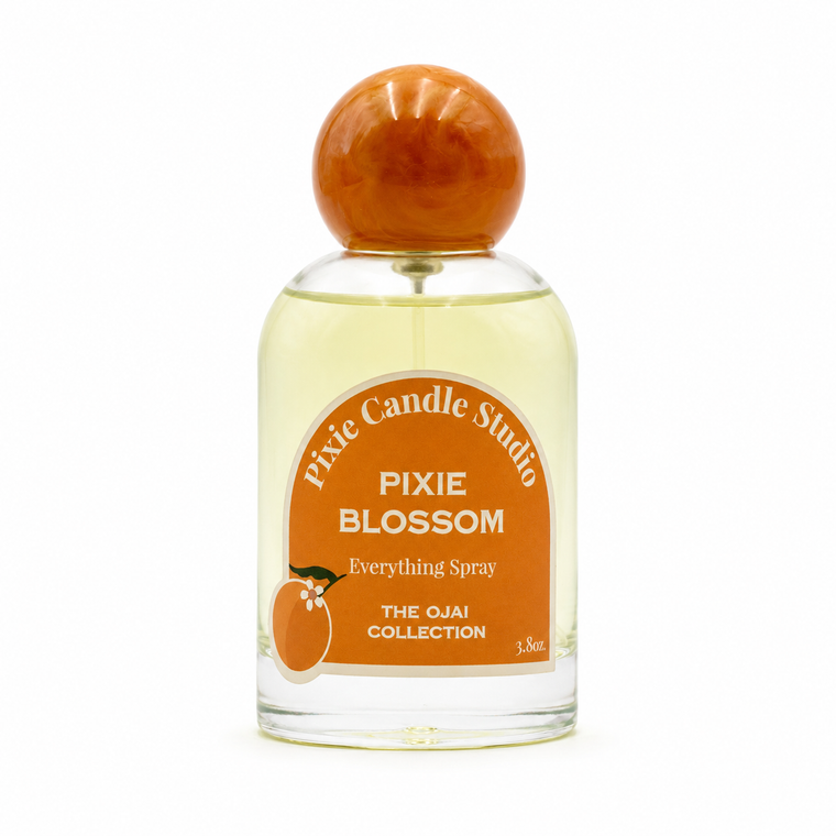 Pixie Candle Studio Pixie Blossom Everything Spray in a clear glass bottle with a round orange wooden cap and an orange label, on a white background.