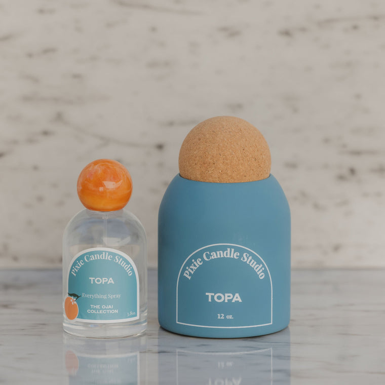 Two bottles from Pixie Candle Studio on a light wooden surface with a neutral background