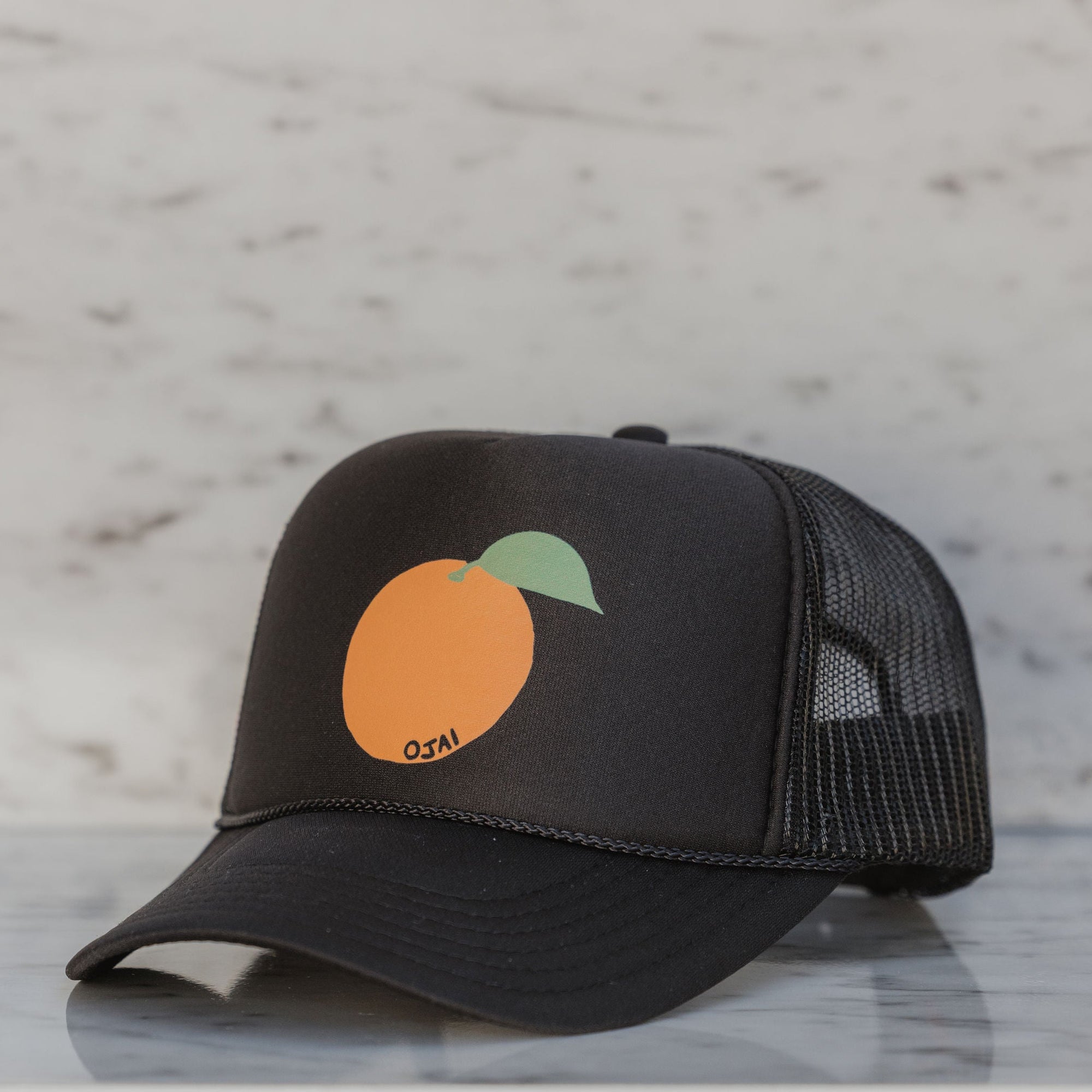 Black trucker cap with an orange and green leaf design on a marble surface