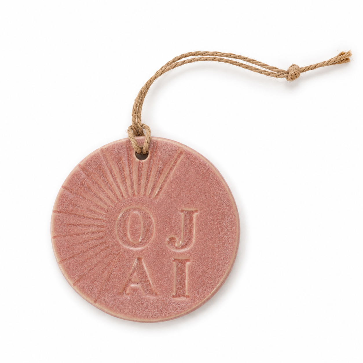 A round terracotta-colored ceramic ornament featuring the embossed text 'OJAI' with a sunburst design, hanging from a natural jute string on a white background.
