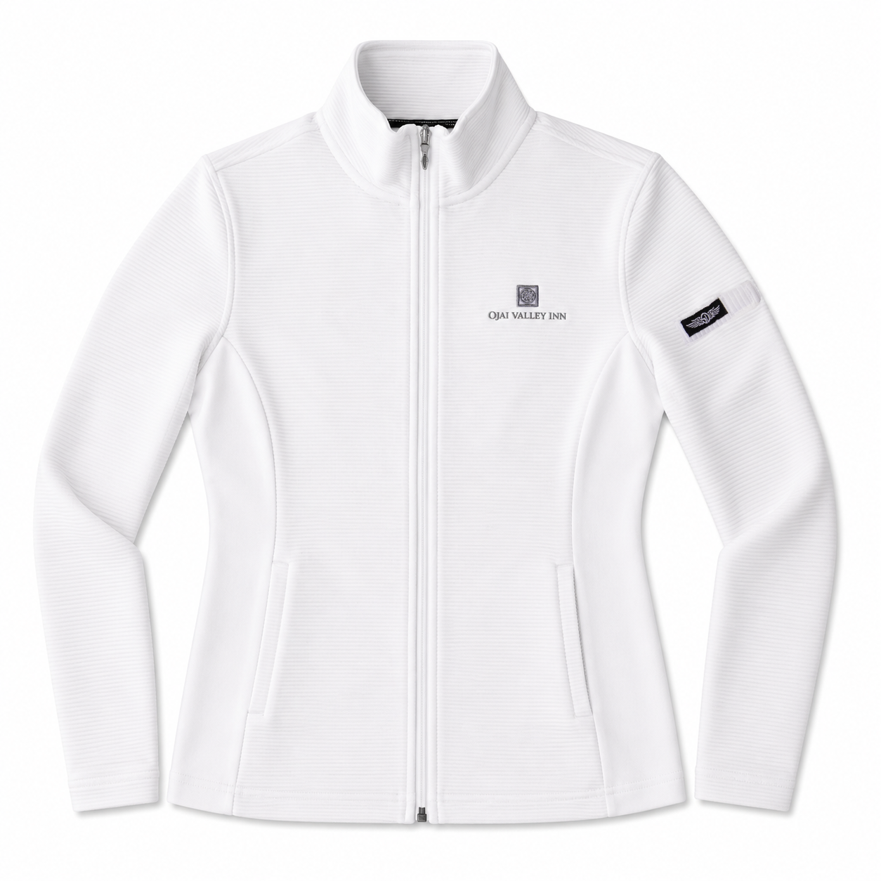 A white long-sleeve zip-up jacket with a stand-up collar, featuring a small 'CMA VALLEY 2026' logo on the left chest and a black brand patch on the right sleeve, shown against a plain white background.