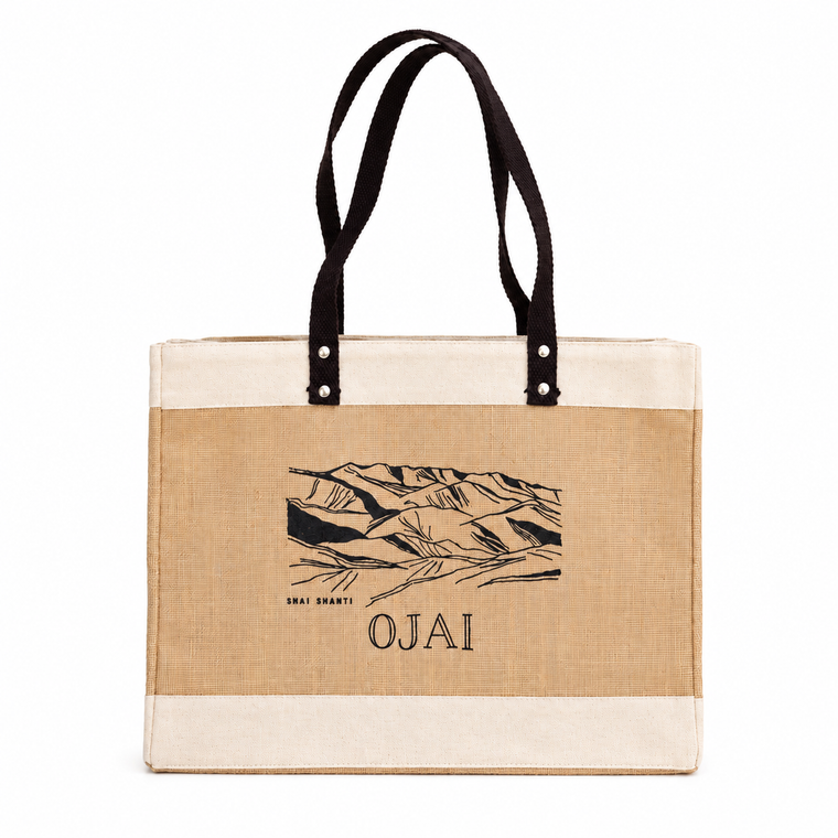 A canvas tote bag with a natural beige body, cream-colored top and bottom bands, and black handles. The center features a black graphic of mountains with the text 'SHAI SHANTY' and 'OJAI' printed below.