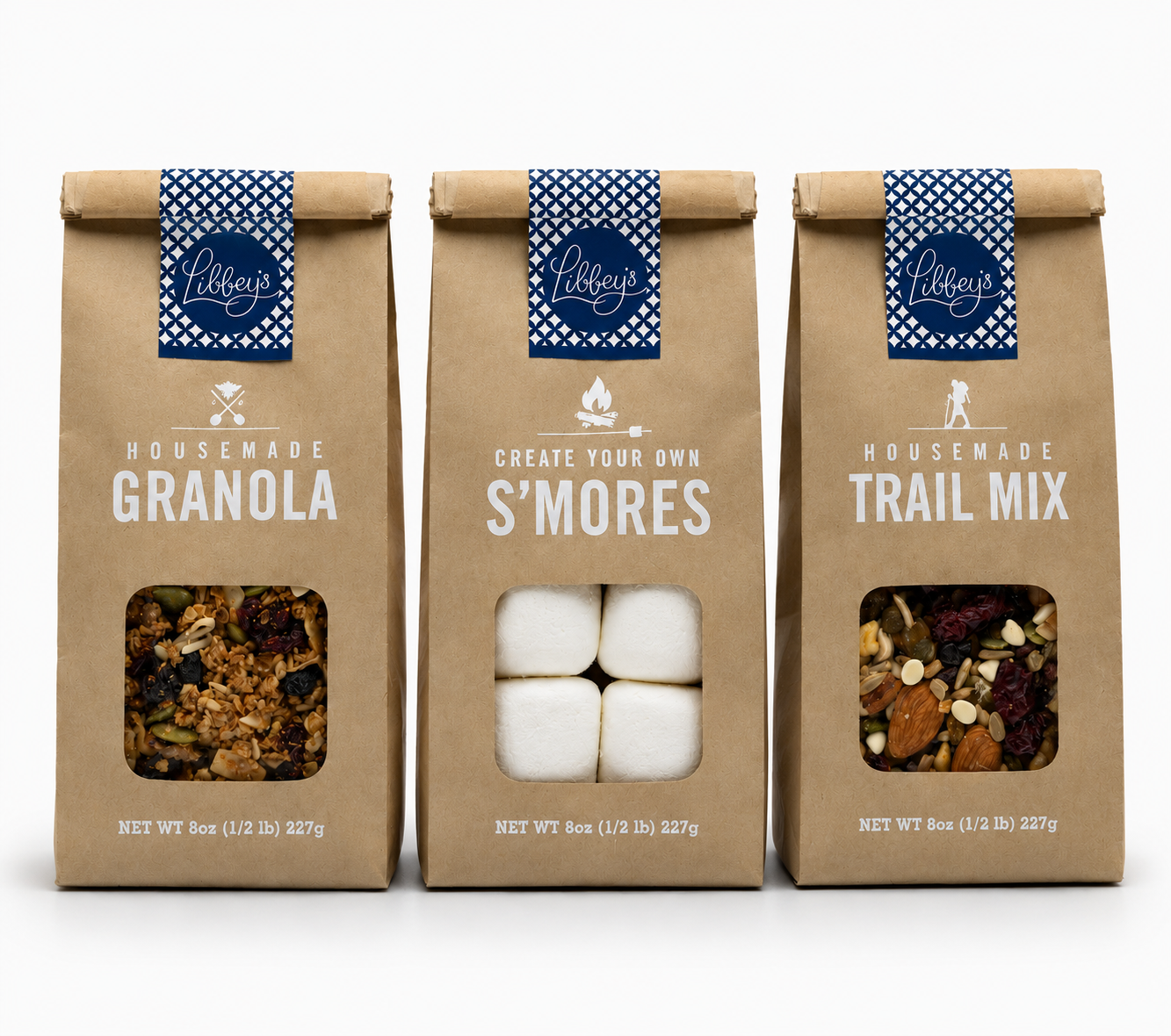 Three kraft paper bags of Libby's housemade granola mixes displayed side-by-side on a white background. The bags feature blue patterned bands with the Libby's logo and display clear windows showing the contents: a granola mix, white marshmallows for s'mores, and a trail mix.