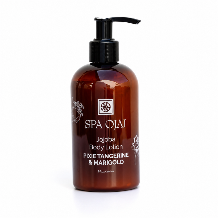 A bottle of SPA OJAI Jojoba Body Lotion in Pixie Tangerine & Marigold scent, featuring an amber brown bottle with a black pump dispenser, set against a plain white background.