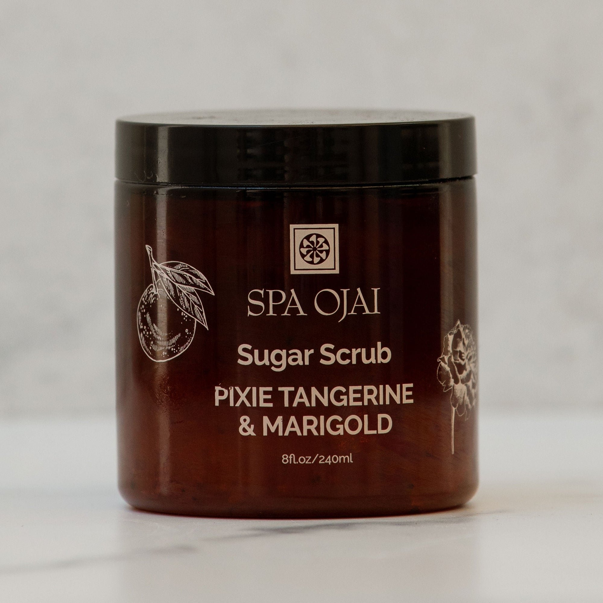 brown spa ojai sugar scrub jar that says pixie tangerine and marigold 8 oz against a neutral backgound