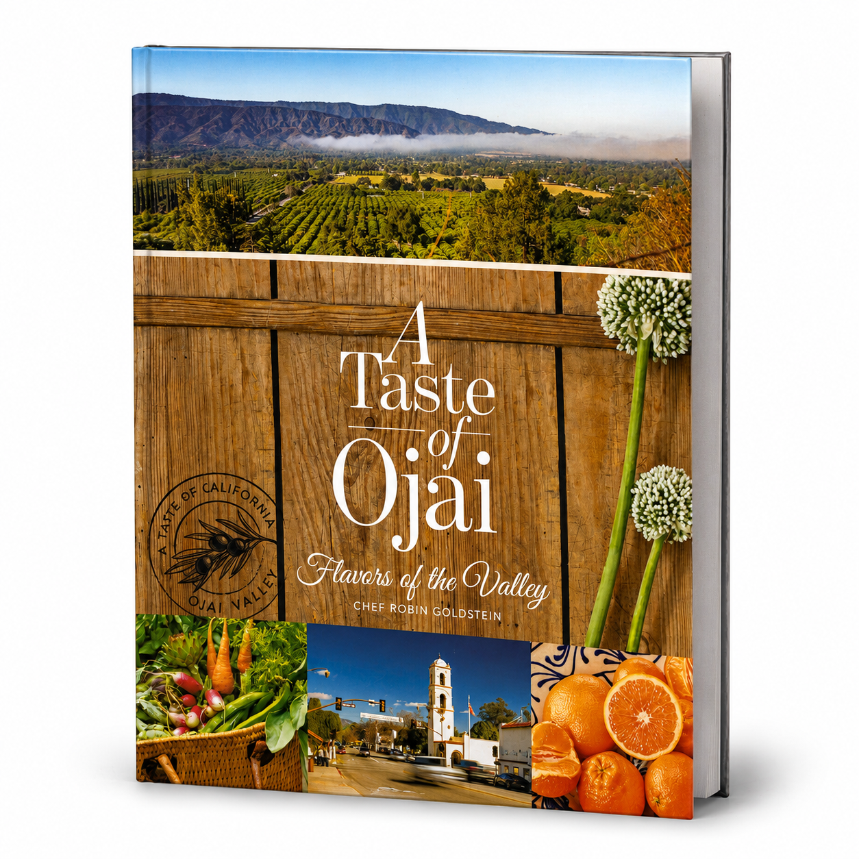 A hardcover cookbook titled "A Taste of Oùai: Flavors of the Valley" by Chef Robin Goldstein, shown standing upright on a white background. The cover features a scenic vineyard landscape, a rustic wooden fence, produce, a street sign, and oranges.